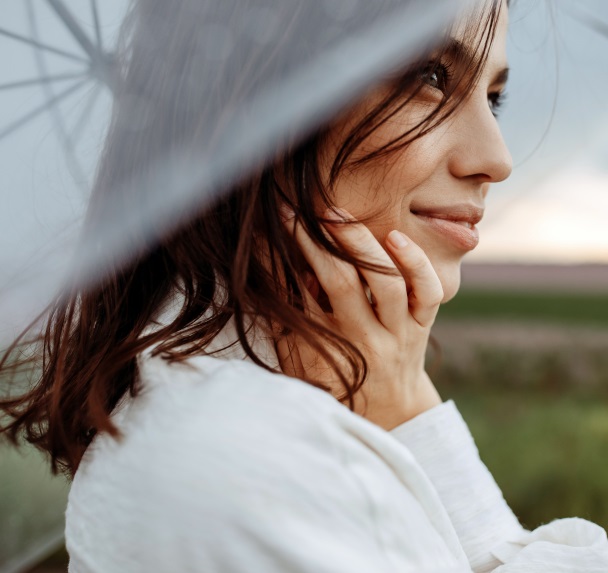 Close-up portrait of a young woman smiling, holding a clear, transparent umbrella, on a dark sky background.